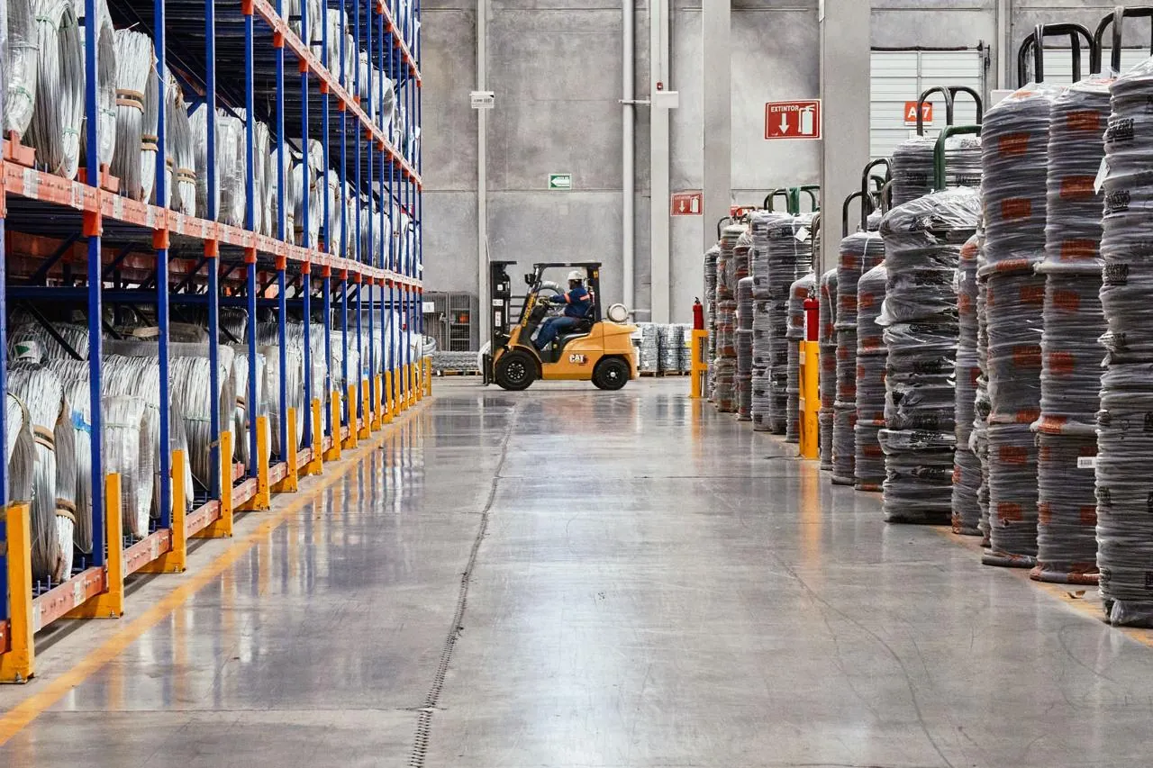 Forklift moving between tall storage racking and coiled stock in a distribution warehouse aisle