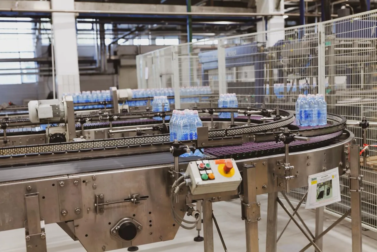 Automated bottling and packaging conveyor line moving filled plastic bottles through a factory